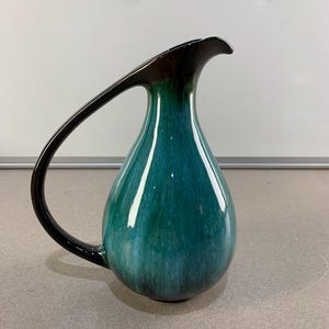 以下が含まれることがあります： 長く湾曲したハンドルが付いた、ティールと黒のセラミックピッチャー。ピッチャーは光沢のある仕上がりで、しずく型をしています。ハンドルとピッチャーの上部は黒で、本体はティールから濃い色合いに変化しています。