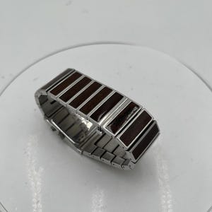 May include: A silver bracelet featuring dark brown wooden rectangular inlays. The bracelet is constructed from linked metal segments, with the wooden sections providing a contrasting texture and colour.
