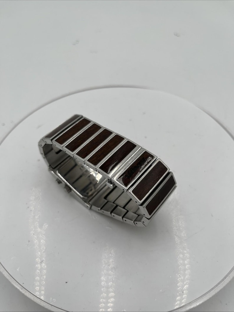 May include: A silver bracelet featuring dark brown wooden rectangular inlays. The bracelet is constructed from linked metal segments, with the wooden sections providing a contrasting texture and colour.
