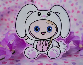 May include: A sticker featuring a cartoon character in a white bunny costume with pink accents. The character has blue eyes, a blonde braid, and a smiling expression. The background is a pink and purple floral design.