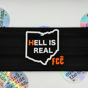May include: Black headband with the text "HELL IS REAL" inside an outline of the state of Ohio. The letters "FCC" are below the Ohio outline. Iridescent stickers with text are in the background.