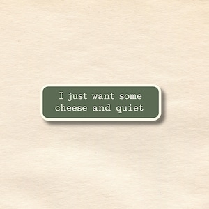 Peut inclure: Un autocollant rectangulaire aux coins arrondis, avec le texte blanc "I just want some cheese and quiet" sur un fond vert fonc&eacute;. L'autocollant a une bordure blanche et est pos&eacute; sur un fond textur&eacute; blanc cass&eacute;.