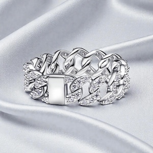 以下が含まれることがあります： シルバーカラーのリング。チェーンリンクのデザインで、小さな透明な宝石がちりばめられています。白いシルクのような表面に展示されています。