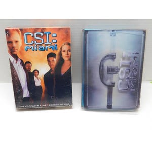 以下が含まれることがあります： テレビ番組「CSI：マイアミ」のDVD2枚組。最初のDVDケースには、番組タイトルが青と黄色で表示されたキャスト写真が掲載されています。2番目のケースは透明で、番組のロゴが入っています。