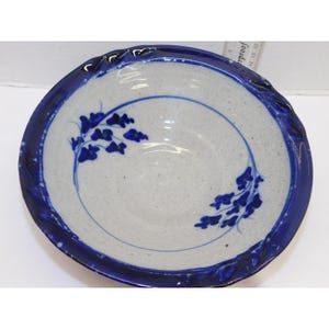 May include: A handmade ceramic bowl with a speckled white interior and a deep blue rim. The rim has a textured, wavy design. Blue floral patterns are painted on the interior. A ruler is visible in the background.