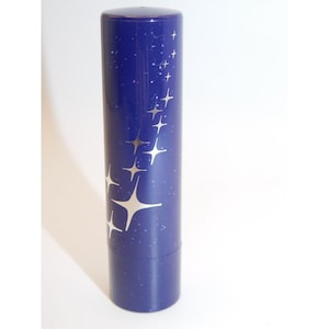 Puede incluir: Un recipiente cilíndrico azul cobalto con un patrón de estrellas plateadas. El recipiente tiene una tapa y una base a juego. El diseño presenta una constelación de estrellas plateadas y pequeños puntos, creando un tema celestial.