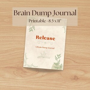 Op de afbeelding: Een afdrukbaar Brain Dump Journal met het woord "Release" in oranje script. Het journal is 21,6 x 27,9 cm groot en heeft decoratieve groene botanische elementen. De omslag heeft de tekst "A Brain Dump Journal".