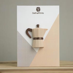 May include: A beige coffee maker with a brown handle and band is displayed on a white, gray, and peach-colored background. The brand name "DefinePrints" is printed in brown at the top. The coffee maker is a three-dimensional design.