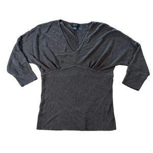 May include: A dark gray V-neck top with three-quarter sleeves. The top has a fitted waist and a relaxed fit through the shoulders and sleeves. The fabric appears to be a soft knit material.