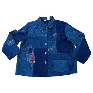 May include: A blue patchwork jacket with a button-down front and a collared neckline. The jacket features embroidered details, including Christmas trees, hearts, and snowflakes. It has a single pocket and long sleeves.
