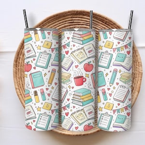 May include: Three white insulated tumblers with black straws, each covered in a colorful school-themed pattern. The pattern includes books, apples, pencils, and notebooks. The tumblers are displayed in a woven basket.