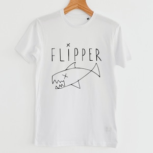 Może przedstawiać: Biała koszulka z czarną grafiką rekina i napisem "FLIPPER" powyżej. Ilustracja rekina ma "X" jako oko i poszarpane zęby.