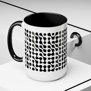 May include: A white ceramic mug with a black handle and the text "But First, Coffee" in a handwritten style. The mug is on a white surface. The mug is approximately 10 cm tall.