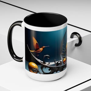 May include: A white ceramic mug with a black interior and a black handle. The exterior features a printed graphic of an orange hummingbird in flight, a large yellow sphere, and intricate black scrollwork against a dark blue background.