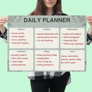 May include: A daily planner poster held by a person. The poster has a light green background with the words "DAILY PLANNER" at the top. It is divided into sections for each day of the week, with space for notes. The planner includes a list of tasks for each day.