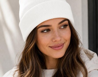 May include: A solid white beanie hat featuring a ribbed knit texture and a wide, folded cuff. The hat is constructed from a soft, opaque material and sits snugly on the head, providing full coverage with a clean, uniform appearance.