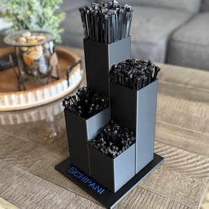 May include: A tiered, black organizer filled with black cable ties. The organizer has three sections of varying heights, each holding a bundle of ties. The base of the organizer has the word "SCHIPANI" in blue.