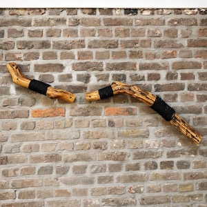 May include: Two natural wood branches mounted horizontally, each featuring sections wrapped in thick black cord. The wood displays a light brown, textured grain with visible knots and small pre-drilled holes at the ends of each branch segment.