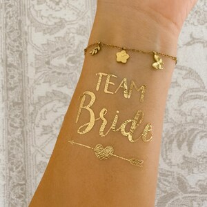 Goldene Team Bride und Bride Tattoos, Tattoos für Junggesellinnenabschied, Bachelorette Party und Hochzeit. Perfekte Accessoires für Braut und Team, glänzende goldene Tattoos für Fotoshooting, Partydeko und Brautparty. Einfache Anwendung, hautfreundlich und wasserfest – ideal als JGA Accessoires, Bridal Shower Tattoo Sticker, Hochzeitsdeko oder Geschenkidee für die Braut und ihre Mädels. JGA Zubehör, Klebetattoos