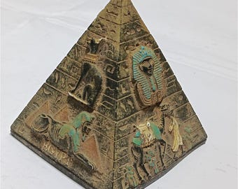 Könnte beinhalten: Dekorative Pyramidenfigur mit Reliefschnitzereien ägyptischer Figuren und Hieroglyphen. Die Pyramide ist hauptsächlich braun mit schwarzen und türkisfarbenen Akzenten. Das Wort "EGYPT" ist auf der Basis zu sehen.