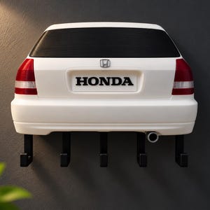 Peut inclure: Un porte-clés mural blanc en forme de l'arrière d'une voiture Honda à hayon. Il présente une lunette arrière noire, des feux arrière rouges et blancs, un emblème Honda, une plaque d'immatriculation HONDA, un pot d'échappement et cinq crochets noirs.