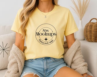 May include: A light yellow t-shirt with the text "Abs Mockups" in a black circular design. The model is wearing denim shorts and a beige cardigan. The image is a mockup for apparel.