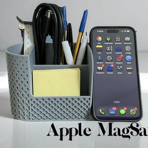 Peut inclure: Un organiseur de bureau gris avec des stylos, des crayons et une règle. Un bloc-notes jaune est dans l'organisateur. Un smartphone noir avec un étui noir est à côté de l'organisateur. Le texte "Apple MagSafe" est en bas.
