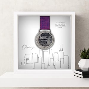 May include: A framed Chicago Marathon medal with a purple ribbon. The silver medal hangs in front of a white background with a black line drawing of the Chicago skyline. Text includes the date and runner's name.