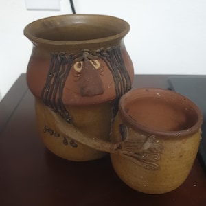 Könnte beinhalten: Ein Set aus drei Keramikbechern mit gesprenkelter, matter Oberfläche. Die Becher sind in Creme-, Hellgrau- und Dunkelgrautönen gehalten. Jeder Becher hat ein schlichtes, minimalistisches Design und einen abgerundeten Henkel.