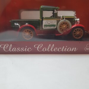 May include: A miniature green and red classic pickup truck with gold-colored wheels and a white spare tire. The truck has the text "PST Pacific Sports Turf" on the side. The words "Classic Collection" are printed below the truck.