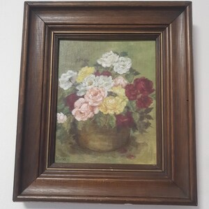 May include: A framed floral still life painting featuring a bouquet of roses in shades of white, pink, yellow, and red. The flowers are arranged in a golden-colored vase against a green background. The painting is signed "Vivian" in the lower left corner.