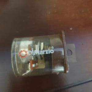以下が含まれることがあります： 白と赤のDiMarzioロゴが入った透明な長方形のギターピックアップ。ピックアップは濃い茶色のベースで、透明なケースを通して内部コンポーネントが見えます。デザインには取り付け穴が含まれています。