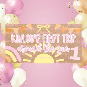 May include: A banner with the text "Kinley's First Trip Around the Sun 1" in pink and yellow, with a rainbow and sun design. The banner is surrounded by pink and gold balloons, confetti, and a pink background.