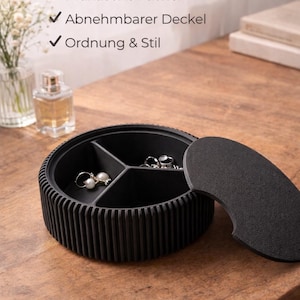 Könnte beinhalten: Schwarzer Schmuck-Organizer mit abnehmbarem Deckel und drei Fächern. Der Organizer steht auf einer Holzoberfläche und trägt den Text "SCHMUCK ORGANIZER". Er enthält Ohrringe und Ringe.