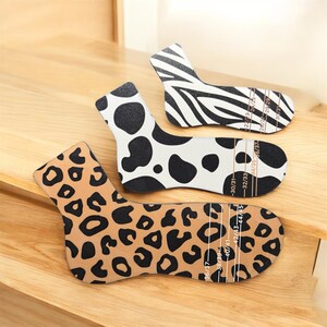 Könnte beinhalten: Drei Socken-Größenführungen mit Tiermotiven. Eine hat einen Leopardenmuster, eine andere einen Kuhdruck und die dritte einen Zebradruck. Jede Führung hat Messmarkierungen in cm.