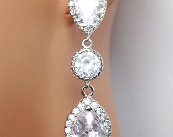 May include: Silver dangle earrings with three clear pear-shaped crystals. The crystals are set in a silver frame with smaller crystals surrounding them.