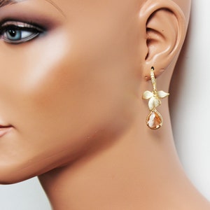 May include: Gold-toned drop earrings featuring a floral design with a pear-shaped, peach-colored gemstone. The earrings have a lever back closure and are displayed on a mannequin.