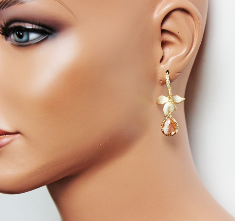 May include: Gold-toned drop earrings featuring a floral design with a pear-shaped, peach-colored gemstone. The earrings have a lever back closure and are displayed on a mannequin.