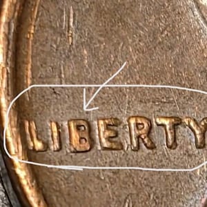 Può includere: Una vista ravvicinata di una moneta da un centesimo degli Stati Uniti color rame con la parola LIBERTY in rilievo in lettere maiuscole. Un cerchio bianco disegnato a mano circonda la parola e una freccia bianca punta alla lettera B di LIBERTY.