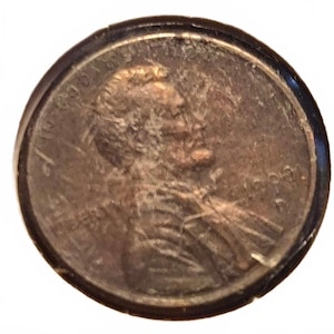 Può includere: Una moneta circolare color rame da un centesimo degli Stati Uniti che presenta il profilo di Abraham Lincoln rivolto verso destra. La moneta mostra il testo In God We Trust lungo il bordo superiore, la parola Liberty a sinistra e l'anno 1991 a destra.