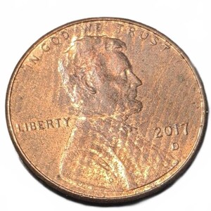 May include: A copper-colored United States one-cent coin featuring the profile of Abraham Lincoln facing right. The text IN GOD WE TRUST is arched at the top, LIBERTY is on the left, and the year 2017 with a D mint mark is on the right.