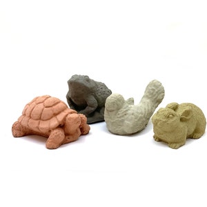 May include: Four small, decorative animal figurines: a turtle, a frog, a bird, and a rabbit. The turtle is a reddish-brown color, the frog is gray, the bird is off-white, and the rabbit is tan. All are made of a textured material.