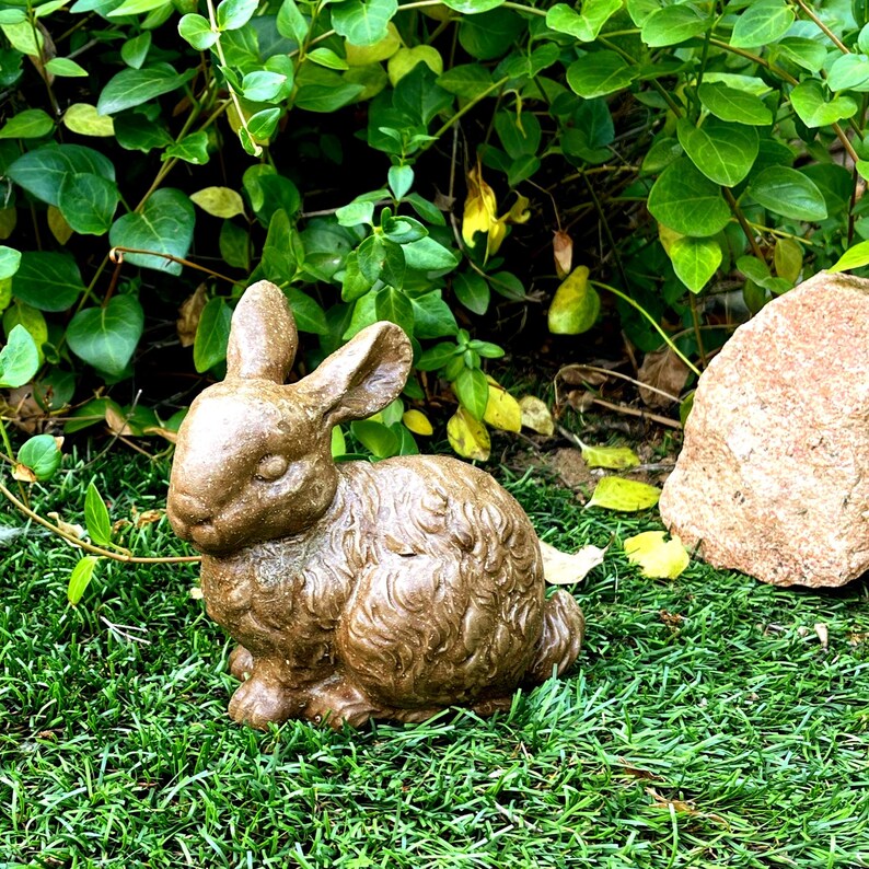 May include: A brown ceramic rabbit figurine with a furry texture. The rabbit is sitting on a green grassy surface.