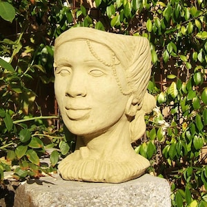 May include: A beige, sculpted head-shaped planter featuring a detailed face with a headband, a delicate chain accessory across the forehead, and hair pulled back. The sculpture has a textured, matte finish and a wide, open top for planting.