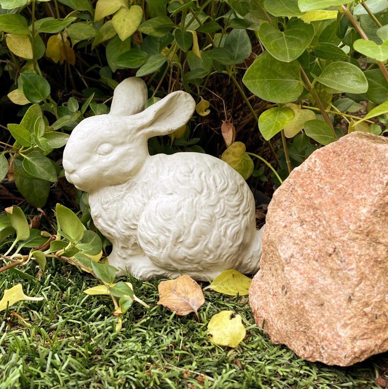 May include: A white rabbit figurine with a textured, curly fur pattern and long ears, positioned in a seated posture. The sculpture features a smooth, matte finish and is crafted with detailed facial features including closed eyes and a small nose.