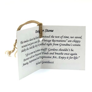 May include: A white card with brown string attached to the top corner. The card has text that reads "Designer Stone" and "This timeless classic had barely survived the test of time, we saved, recreated and gave a new life. Vintage Recreations" are chippy shabby chic, look like they're pulled right from Grandma's estate. "Life is some real serious stuff! Gardens shouldn't be. Decorate with our Treasured Finds and breathe once again. Amusing, Inspirational and Expressive Art...Enjoy it for life!" Michael Gentilucci"