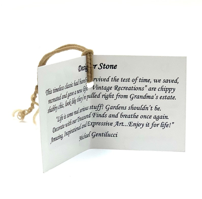 May include: A white card with brown string attached to the top corner. The card has text that reads "Designer Stone" and "This timeless classic had barely survived the test of time, we saved, recreated and gave a new life. Vintage Recreations" are chippy shabby chic, look like they're pulled right from Grandma's estate. "Life is some real serious stuff! Gardens shouldn't be. Decorate with our Treasured Finds and breathe once again. Amusing, Inspirational and Expressive Art...Enjoy it for life!" Michael Gentilucci"