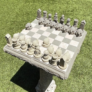 May include: A stone chess set with a gray and white checkered board. The chess pieces are sculpted in a garden theme, including turtles, gnomes, and miniature buildings. The set is mounted on a decorative pedestal, suitable for outdoor use.