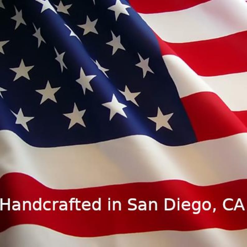 May include: The flag of the United States of America featuring red and white horizontal stripes and a blue canton with white stars. The text Handcrafted in San Diego, CA is printed in white across the lower portion of the fabric surface.