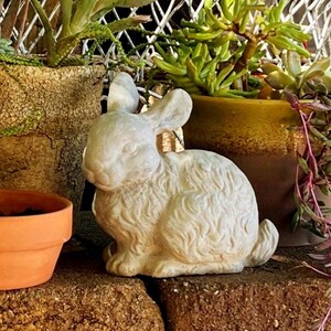 May include: A white, textured rabbit figurine in a seated position with upright ears and detailed fur markings. The sculpture is crafted with a matte finish and displays a realistic posture, capturing the form of a small hare in a neutral tone.